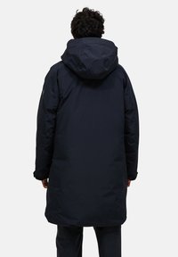 Lång mörk marinblå parka med huva, med en slät yta och en avslappnad passform. Inga synliga mönster eller detaljer i hårdvara.