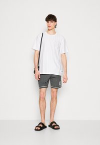 Hvit kortermet T-skjorte med vertikale striper og en hevet '8'-logo, sammen med grå stripete shorts og svarte sandaler.