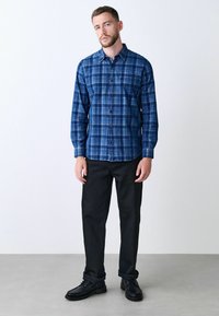 Blau karierte Button-Up-Bluse mit langen Ärmeln, kombiniert mit schwarzen Hosen und schwarzen Schuhen. Verfügt über einen klassischen Kragen und eine gerade Passform.