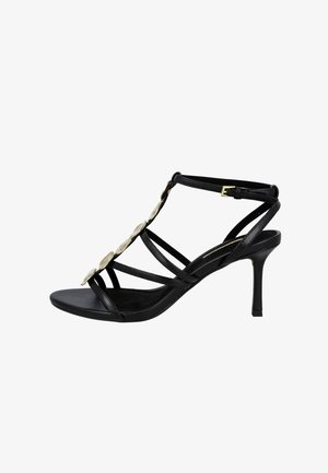 Sandalia negra de tacón alto con tiras y hebilla en el tobillo, con adornos circulares dorados a lo largo de la tira frontal.