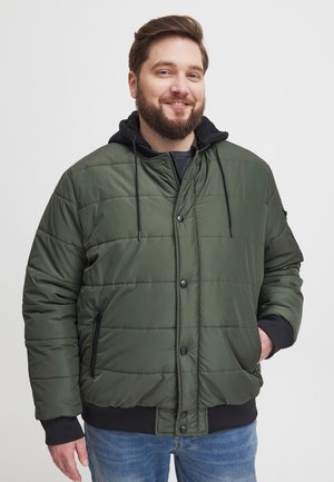 Grøn quiltet jakke med lynlåshætte, trykknapper og sidelommer. Har sorte detaljer ved manchetter og kant, lavet af glat materiale.