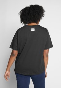 Černé bavlněné tričko s krátkým rukávem, kulatým výstřihem a bílou nášivkou loga Nike vzadu. Nosené s tmavě modrými džíny.