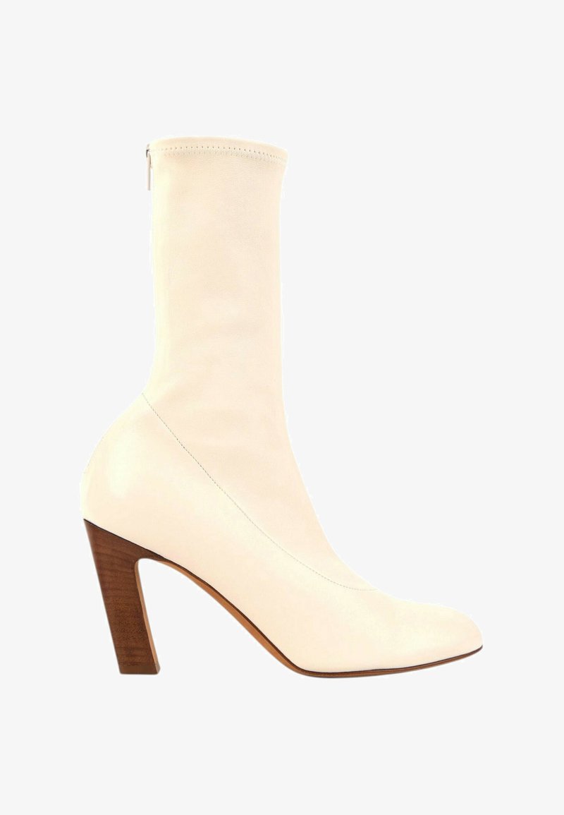 Botte en cuir couleur crème mi-mollet avec bout pointu et talon haut en bloc de bois empilé, fermeture éclair latérale visible à l'arrière.