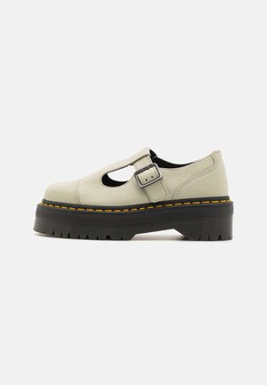 Beige Lederhalbschuhe mit abgerundeter Spitze, seitlichem Ausschnitt und verstellbarem Schnallenverschluss. Dicke schwarze Plateau-Sohle mit gelben Nähten und Gummiprofil.