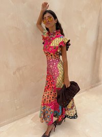 Levendige patchwork midi-jurk met ruches mouwen, multicolore patronen en een hoge kraag. Bruine clutch tas met decoratieve nieten.