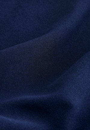 Dunkelblauer Mikrofaserstoff mit einer feinen, strukturierten Oberfläche und weichen Falten, die sanfte Schatten und Lichtreflexe erzeugen.