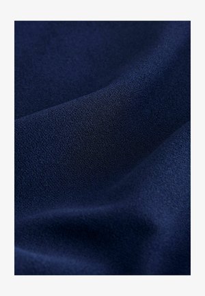 Dunkelblauer Mikrofaserstoff mit einer feinen, strukturierten Oberfläche und weichen Falten, die sanfte Schatten und Lichtreflexe erzeugen.