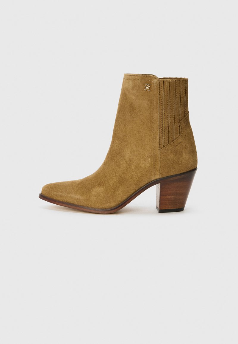 Stivale alla caviglia in suede marrone con punta affusolata, pannello laterale testurizzato e tacco impilato. Presenta un piccolo logo metallico sul davanti.