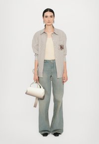Camicia a righe con ricami marroni, canotta beige, jeans a gamba larga azzurri chiari e borsa degradé nei toni crema e grigio.