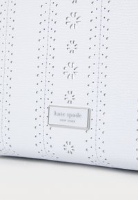 Borsa a mano in pelle bianca con un design perforato, hardware in argento e una placca rettangolare del marchio. Superficie testurizzata con accenti floreali.