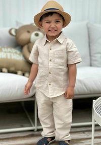 Ljusbeige linne skjorta och byxor, kortärmad med bröstficka, kombinerad med en halmhatt och mörka skor.