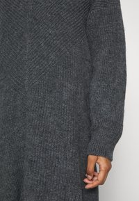 Cardigan en tricot gris foncé avec un motif texturé. Présente des manches longues et une coupe décontractée. Le matériau semble doux et chaud.