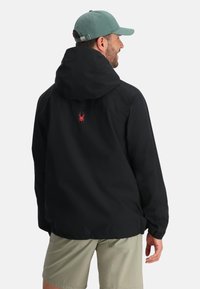 Giacca nera con cappuccio e logo di un ragno rosso sulla schiena; realizzata in materiale impermeabile con una vestibilità comoda e polsini elastici.