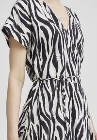 Schwarzes und weißes, zebra-musterndes Kleid mit kurzen Ärmeln, V-Ausschnitt und gebundenem Taillendetail, hergestellt aus leichtem Stoff.