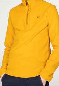 Žlutý fleecový svetr s límcem na půl zip, který má jemné logo, měkkou texturu a dlouhé rukávy. Ideální pro volný čas.