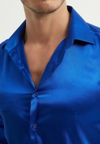 Chemise en satin bleu vif avec une texture lisse, un col pointu et une fermeture à boutons. Brillance visible et design ajusté.