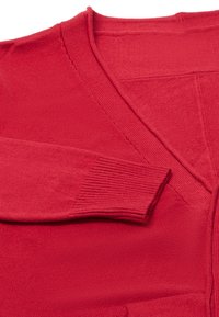 Červený pletený kardigan s výstřihem do V, ribbed manžetami a hladkou strukturou. Látka vypadá měkce a má polo-strukturovaný vzhled.
