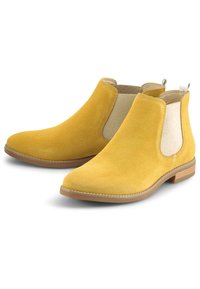 Žluté semišové kotníkové boty s elastickými bočními panely a očkem na zadní straně, s béžovými texturovanými detaily a podrážkou z hnědé gumy.