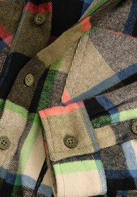 Kostkowana flanela w odcieniach zieleni, czerwieni, czerni i niebieskiego, z kontrastowymi guzikami oraz teksturowanym wykończeniem i nakładającymi się wzorami.