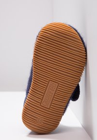 Ciemnoniebieski pantofel z teksturowaną, gumową podeszwą; posiada miękką tkaninę górną i wytłoczone logo marki na podeszwie.