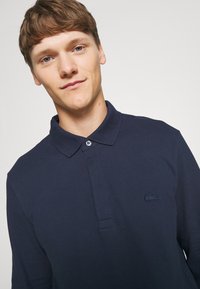 Marinblå pikétröja med knappkrage och en liten broderad logotyp på bröstet. Bomullstextur med klassisk passform.