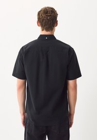 Camicia nera a maniche corte realizzata in cotone. Dotata di colletto con bottoni e chiusura con un solo bottone sul retro. Texture semplice e liscia.