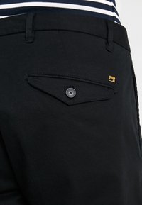Pantaloni neri con una tasca posteriore con bottone e un piccolo dettaglio dorato. Presentano una texture piatta e liscia e un design classico a gamba dritta.