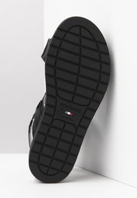 Suola in gomma nera con grip testurizzato, con marchio e informazioni sulle taglie. Progettata con diversi modelli di trazione per una stabilità migliorata.