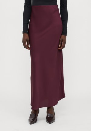Burgundy satin maxi skirt with a smooth texture and a side slit, paired with pointy, glossy, dark shoes, worn with a fitted black top.