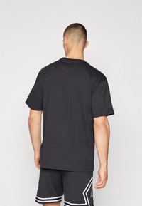 Camiseta de algodón negra de manga corta, con escote redondo y un corte relajado. Se lleva con pantalones cortos deportivos negros que tienen acentos blancos.
