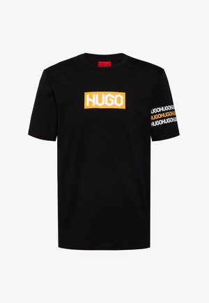 T-shirt noir à manches courtes avec un logo rectangulaire orange "HUGO" sur la poitrine et le texte répété "HUGO" en blanc et orange sur la manche droite.
