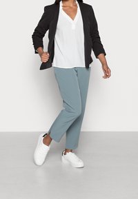 Blazer nero, blouse bianca, pantaloni azzurri chiari con spacchi laterali e sneakers bianche con dettagli neri. Texture lisce e design su misura.