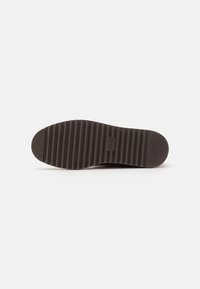 Brown rubber shoe sole with a ribbed texture and a flat profile. Features a logo embedded near the center for branding.