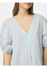 Ljusblå rutig blus med V-ringning, puffärmar och en detaljerad veck fram. Tillverkad av ett mjukt, lätt tyg.