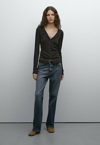 Bruine geribde lange mouwen shirt met knoopdetail, gecombineerd met vervaagde blauwe rechte jeans en beige schoeisel. Eenvoudig, minimalistisch ontwerp.