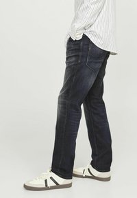 Jeans de denim închis, cu o croială dreaptă, având o ușoară decolorare. Asortați cu adidași albi care au dungi negre.