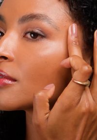 Femme à la peau claire touchant la région des tempes avec les doigts, mettant en valeur un teint lisse et un maquillage naturel.