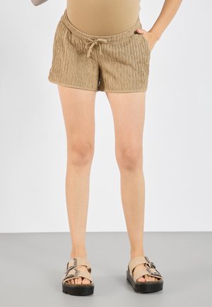 Kvinde iført beige teksturerede shorts med snøre i taljen og beige platformsandaler med to spænder.