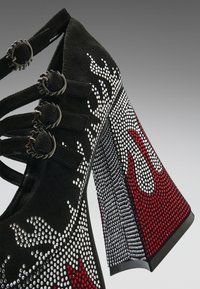 Svart høyhælte sko med flere spenner, dekorert med hvite og røde rhinestones formet som flammer på overdelen og hælen.