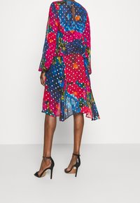 Barevné květinové šaty s dlouhými rukávy, vrstveným designem a puntíkovaným vzorem. Vyrobené z lehkého materiálu, s detaily klíčové dírky na zádech.
