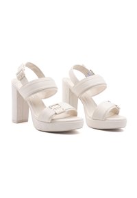 Valkoiset platofrmit sandaalit, joissa on kaksi leveää hihnaa, neliön muotoinen kärki ja tukevat paksut korot. Etuhihnassa on hopeanvärisiä yksityiskohtia.