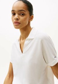 Witte poloshirt met een V-hals en korte mouwen. Gemaakt van gestructuurd stof, met een klein logo-accent op de mouw.