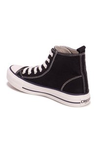 Zapatilla alta de lona negra con cordones y costuras blancas. Presenta una puntera de goma y una suela blanca con un acento en azul marino.