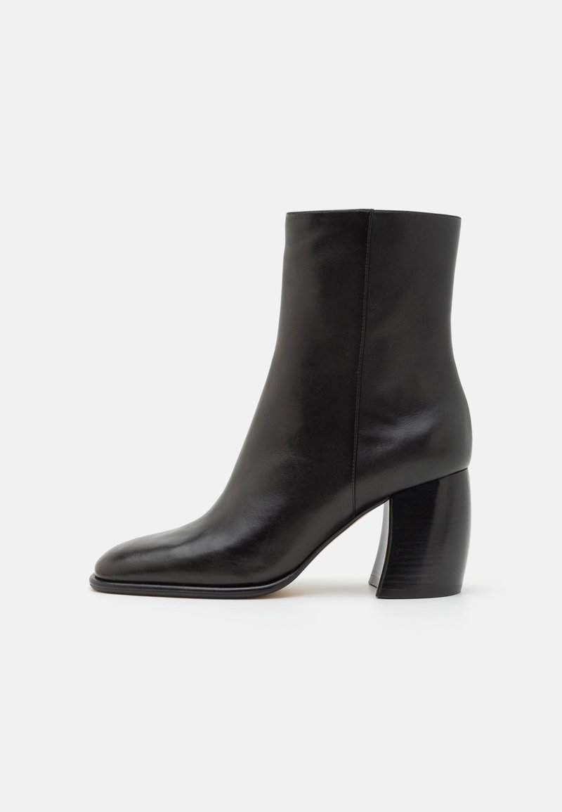 Bottine en cuir noir avec un bout pointu, finition brillante et un talon épais et rond. Texture lisse et design minimaliste.