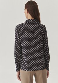 Blusa a maniche lunghe in tessuto blu navy con un piccolo motivo floreale in crema. Il design presenta un collo con una texture liscia.