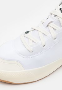 Vit sneakers med slätt textilöverdrag, vita snören och en gummisula. Har subtil sömnad och en yttersula i gummifärg.