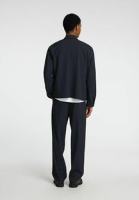 Completo giacca e pantaloni tagliato all'americana. Tessuto liscio, vestibilità rilassata, maniche lunghe e pantaloni a gamba dritta. Design minimalista senza modelli visibili.