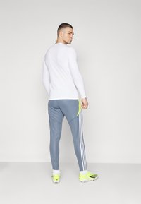 White long-sleeve athletic top paired with gray pants featuring a neon green accent and three white stripes along the side, worn with bright green shoes.