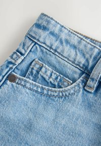 Nærbillede af lyseblå denimjeanslomme med synlige sømme, bæltestrop og en lille møntlomme inde i hovedlommen.