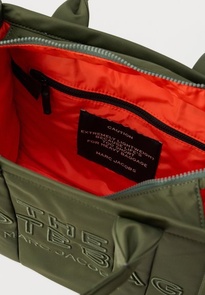 Τσάντα ώμου σε ελαιχρώμα με έντονη πορτοκαλί εσωτερική επένδυση και τσέπη με φερμουάρ, με ετικέτα προειδοποίησης για ελαφρύ ύφασμα από τη Marc Jacobs.